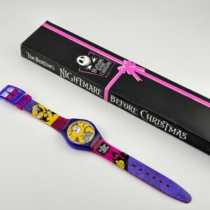 May include: A purple and yellow wristwatch with a digital display featuring Jack Skellington from the movie "Nightmare Before Christmas". The watch comes in a black box with a pink ribbon and the text "Tim Burton's Nightmare Before Christmas".