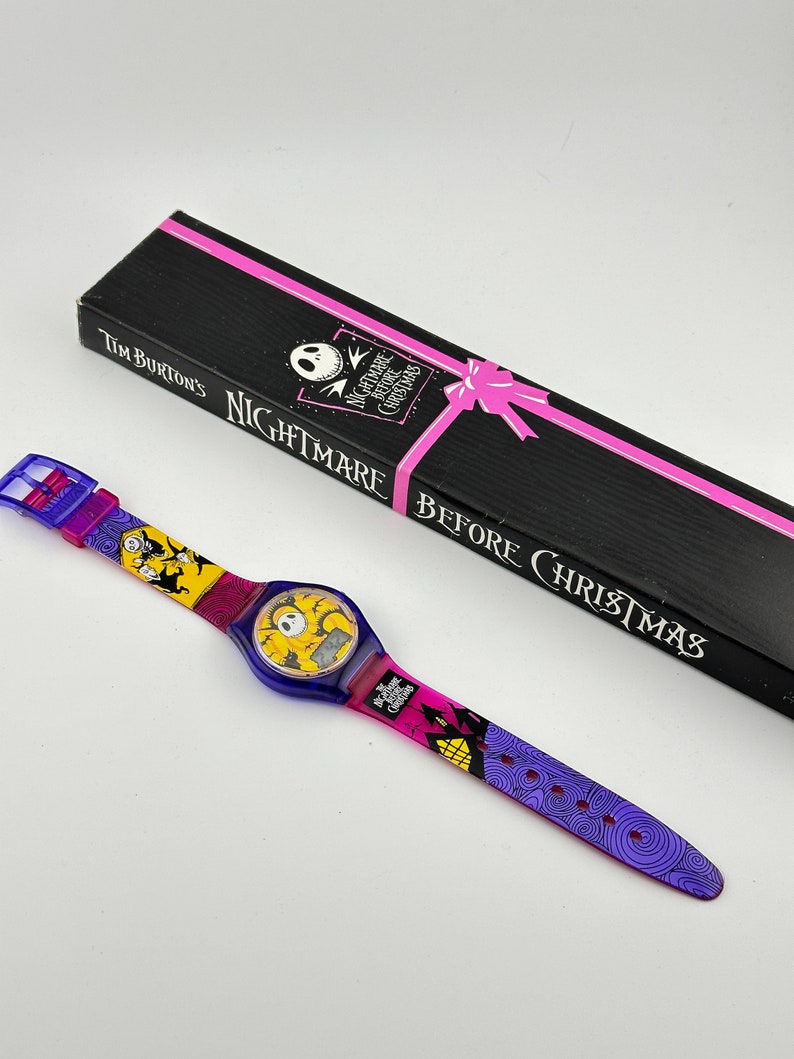 May include: A purple and yellow wristwatch with a digital display featuring Jack Skellington from the movie "Nightmare Before Christmas". The watch comes in a black box with a pink ribbon and the text "Tim Burton's Nightmare Before Christmas".