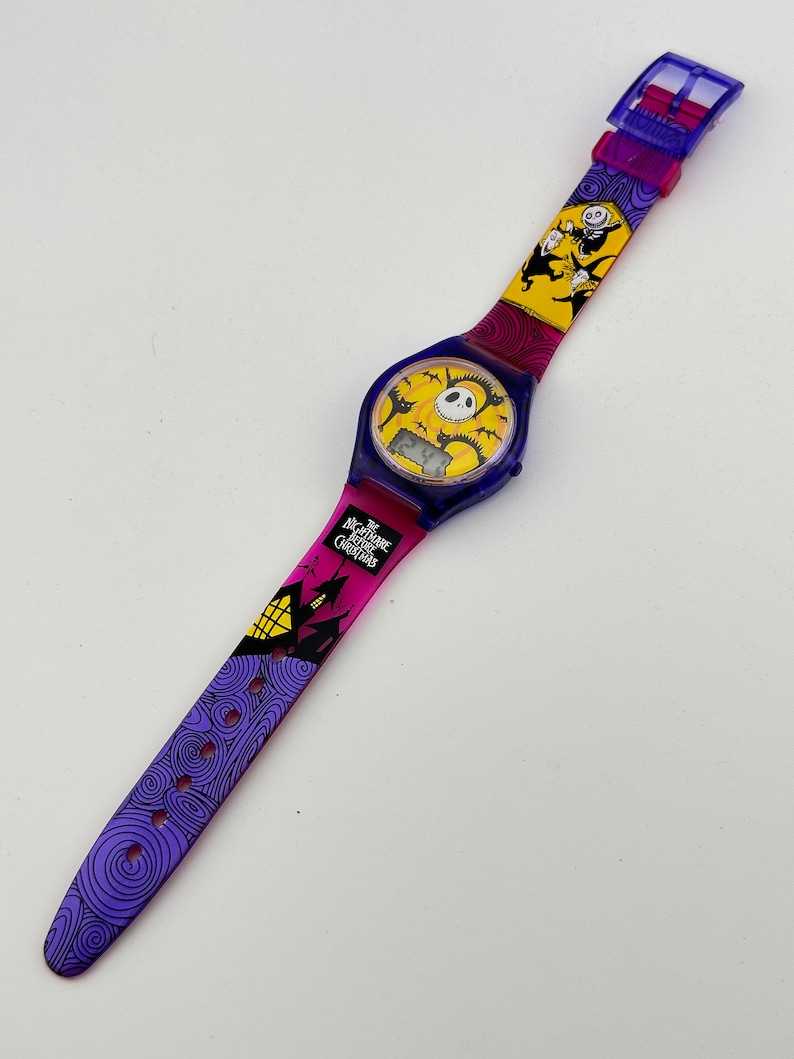 May include: A purple, yellow, and black wristwatch with a digital display and a band featuring characters from The Nightmare Before Christmas. The band has a purple, yellow, and pink gradient.