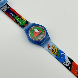 May include: A blue and orange wristwatch with a digital display featuring a Santa Claus character. The watch band has a colorful design with images from the movie "The Nightmare Before Christmas".
