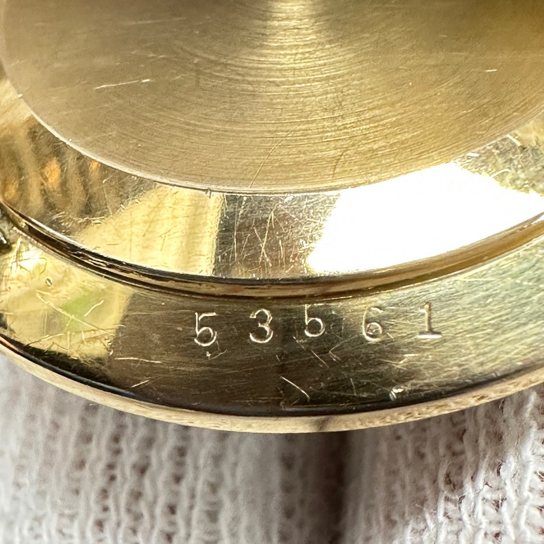 May include: Close-up of a gold-colored watch case with the number 53561 engraved on the bottom.