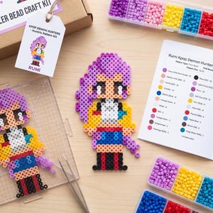 May include: A DIY Rumi Perler bead craft kit featuring a cardboard box, a tag labelled KPOP DEMON HUNTERS, a clear pegboard with a purple-haired character design, a matching finished bead figure, a colour-coded instruction booklet, and plastic bead containers.