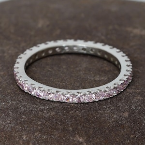 May include: A silver band ring with a row of small pink gemstones around the entire band.