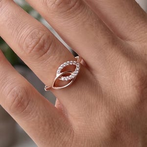 May include: Rose gold ring featuring a double leaf design. One leaf is adorned with small, clear gemstones. The ring is displayed on a hand with manicured nails, showcasing the ring's delicate details and elegant style.