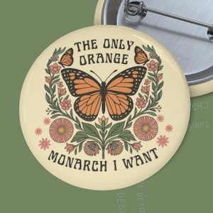 Pode incluir: Um botão redondo creme com um design de borboleta monarca laranja e preta, rodeado por elementos florais. O texto diz "THE ONLY ORANGE MONARCH I WANT". Um segundo botão é visível.