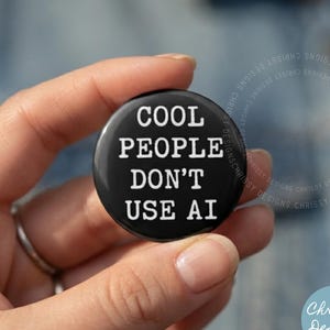 Puede incluir: Un botón redondo de color negro con el texto blanco "COOL PEOPLE DON'T USE AI" en una fuente negrita sin remates. El botón tiene un acabado liso y brillante, diseñado para ser colocado en prendas de vestir o accesorios como un distintivo.