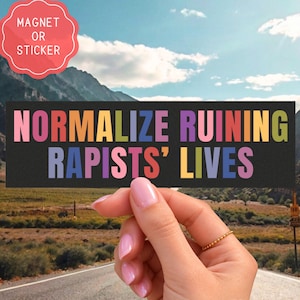 Könnte beinhalten: Ein rechteckiger schwarzer Aufkleber oder Magnet mit dem Text "NORMALIZE RUINING RAPISTS' LIVES" in mehrfarbigen, fetten, serifenlosen Großbuchstaben. Der Text ist in zwei Zeilen auf einem einfarbigen schwarzen Hintergrund angeordnet, wobei jeder Buchstabe farbig ist.