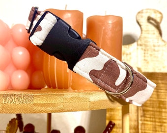 May include: A brown and white camouflage dog collar with a black plastic buckle and a silver metal D-ring.