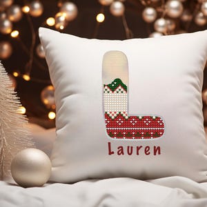 May include: White pillow with a red, green, and white stocking embroidered on it. The stocking is shaped like the letter L and the name "Lauren" is embroidered below it.