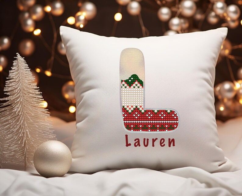 May include: White pillow with a red, green, and white stocking embroidered on it. The stocking is shaped like the letter L and the name "Lauren" is embroidered below it.