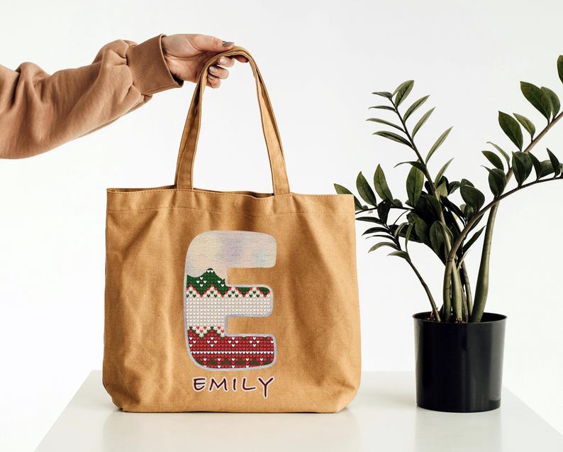 May include: A brown canvas tote bag with a red, green, and white patterned letter "E" and the name "Emily" written below.