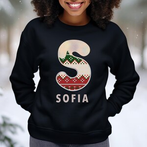 May include: Black sweatshirt with a white and red knit letter "S" and the name "SOFIA" printed below. The letter "S" has a green and white knit pattern.
