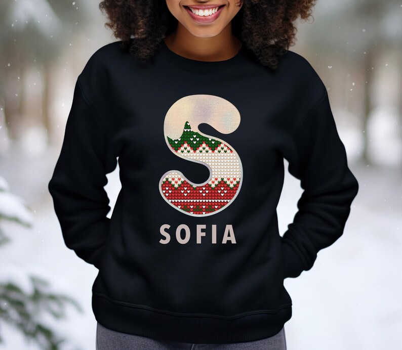 May include: Black sweatshirt with a white and red knit letter "S" and the name "SOFIA" printed below. The letter "S" has a green and white knit pattern.