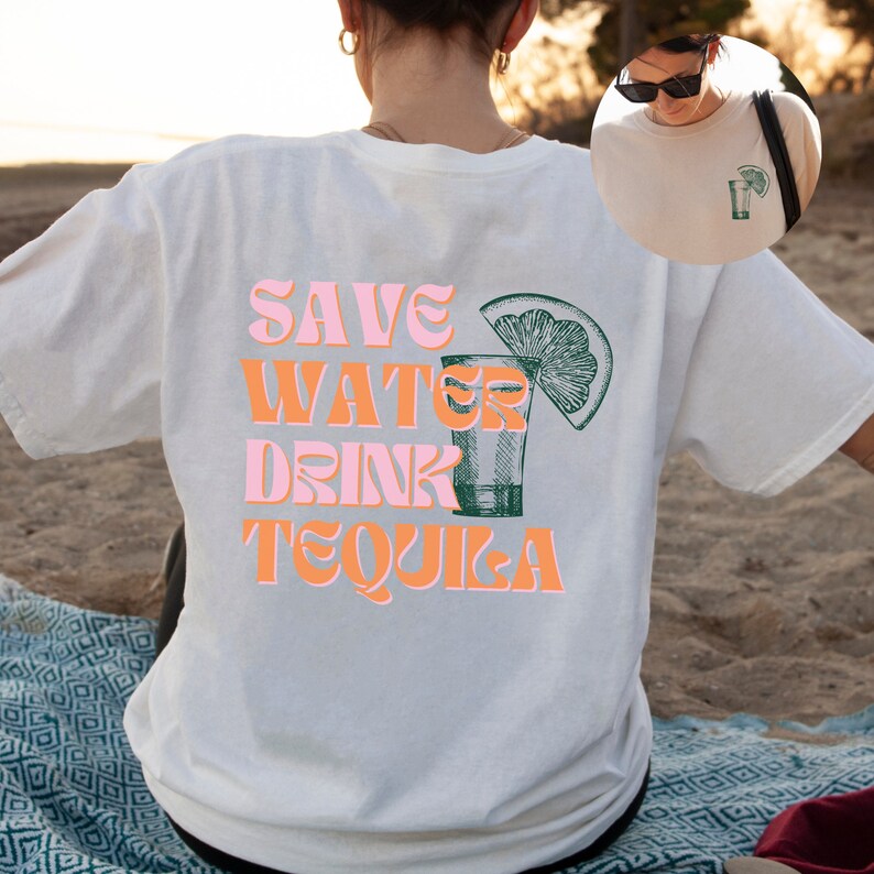 Pu&ograve; includere: Maglietta bianca con il testo "SAVE WATER DRINK TEQUILA" in lettere rosa e arancioni. Accanto al testo c'&egrave; un'illustrazione verde e bianca di un bicchierino con una fetta di lime.