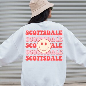 May include: White sweatshirt with a pink and red graphic design that says "SCOTTSDALE" five times with a smiley face in the middle.