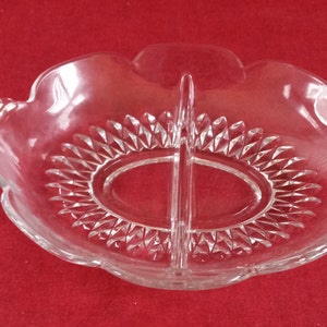 Puede incluir: Un plato de servir dividido de vidrio transparente con un borde festoneado y recortes en forma de diamante. El plato tiene dos secciones y dos asas.