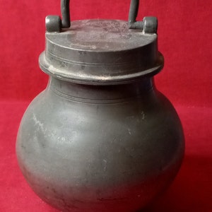 May include: A pewter jar with a lid and a handle. The jar is round and has a bulbous shape. The jar is gray in color and has a smooth surface.