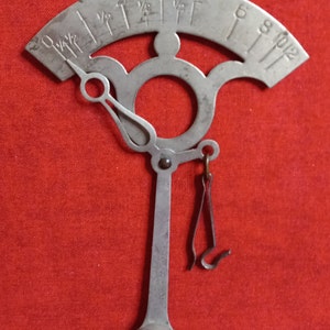 May include: A silver-toned hanging scale with a circular dial and a long, thin arm. The dial has markings for ounces and pounds. The arm has a hook at the end for hanging items.