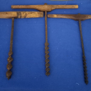 May include: Four antique hand-crank wood augers with wooden handles. The augers are made of metal and have a spiral design. The handles are made of wood and are attached to the augers with metal brackets.