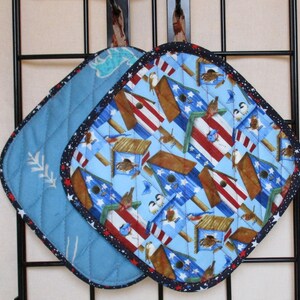 Könnte beinhalten: Zwei gequiltete Topflappen aus blauem und weißem Stoff. Ein Topflappen hat ein Muster aus Vogelhäusern mit roten, weißen und blauen Streifen. Der andere Topflappen hat ein einfaches blaues und weißes Muster.