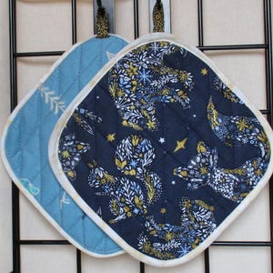 Könnte beinhalten: Zwei gequiltete Topflappen, einer blau mit weißen Nähten und der andere dunkelblau mit einem weißen und goldenen Blumenmuster.