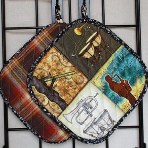 Puede incluir: Dos agarraderas de olla acolchadas con un tema musical. Una agarradera presenta un patrón de cuadros en tonos marrones, rojos y negros. La otra agarradera presenta un collage de instrumentos musicales, incluyendo un trombón, una trompeta y tambores, con un fondo de notas musicales y partituras.