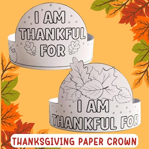 May include: Two white paper crowns with the text "I AM THANKFUL FOR" in black. One crown has leaf and apple illustrations, the other has leaf illustrations. The words "THANKSGIVING PAPER CROWN" are at the bottom.