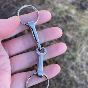 May include: A silver metal snaffle bit with two rings. The bit is designed for use with a horse's bridle.