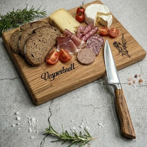 May include: A wooden charcuterie board with various cheeses, sliced meats, bread, and tomatoes. A stainless steel knife with a wooden handle rests on the board. The word "Vesperbrett" is etched on the board.