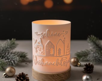 May include: A white cylindrical candle holder with a wooden base, featuring a cut-out design of houses, trees, and the text "Schöne Weihnachtszeit". The candle holder is illuminated from within, creating a warm glow. Christmas decor.