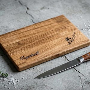 May include: A rectangular wooden cutting board with the word "Vesperbrett" engraved on it, along with a small illustration. A stainless steel knife with a wooden handle rests beside the board. Thyme sprigs and salt are also present.
