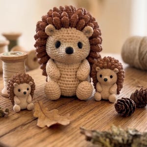 Peut inclure: Trois figurines de hérissons au crochet de tailles différentes, avec des visages et des corps couleur crème et des dos marron texturés. Chaque hérisson a de petits yeux noirs et un nez noir. Le texte Ki-generierte Inhalte est visible.