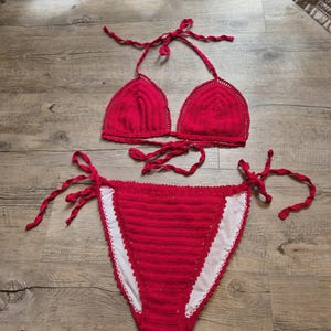 May include: Red crochet bikini top and bottom with thin straps. The top is a triangle style and the bottom is a high-cut style with ties on the sides.