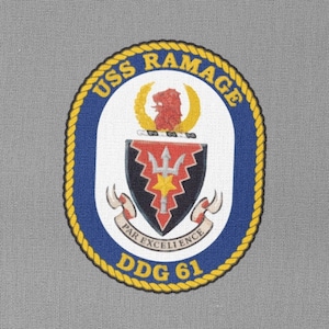 Könnte beinhalten: Ein blauer und goldener runder Aufnäher mit dem Text "USS RAMAGE DDG 61" und einem Wappen mit einem Dreizack und einem Stern. Der Text "PAR EXCELLENCE" ist auf einem Band unter dem Wappen geschrieben.