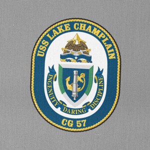 以下が含まれることがあります： 縁に「USS LAKE CHAMPLAIN」という文字が書かれた青と金の円形のワッペン。円の内側には、船の錨、大砲、そして「INGENUITY」、「DARING」、「DISCIPLINE」という文字が書かれた紋章があります。「CG 57」という文字はワッペンの下部に書かれています。