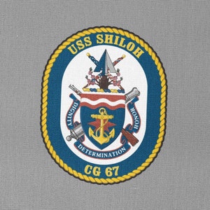 Könnte beinhalten: Ein blauer und goldener runder Patch mit dem Text "USS SHILOH CG 67" und einem Wappen mit einem Anker, gekreuzten Kanonen und den Worten "DIGNITY, DETERMINATION, HONOR".