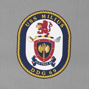 Könnte beinhalten: Ein grauer Aufnäher mit einem marineblauen und goldenen runden Emblem. Das Emblem zeigt einen roten Löwen, einen Schild mit einer gekreuzten Axt und einem Dreizack sowie den Text "USS MILIUS DDG 69".