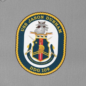 May include: An embroidered patch featuring the USS Jason Dunham crest. The crest is an oval shape with a navy blue border and gold trim. The words "USS JASON DUNHAM" are at the top, and "DDG 109" at the bottom.