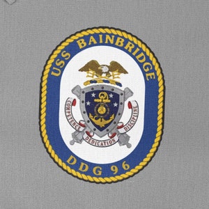 May include: An embroidered patch with the words "USS BAINBRIDGE DDG 96". The patch is navy blue, gold, and white, and features a detailed emblem with an eagle, anchor, and the words "Competence, Dedication, Discipline".