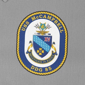 Può includere: Toppa circolare con la scritta "USS McCampbell" in blu e oro. La toppa presenta uno scudo centrale con un motivo blu e bianco, una croce dorata e la scritta "Relentless in Battle" e "DDG 85".