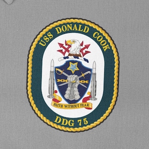 May include: A navy blue and gold embroidered patch with the text "USS DONALD COOK DDG 75" and a crest featuring an eagle, crossed swords, and the text "FAITH WITHOUT FEAR".