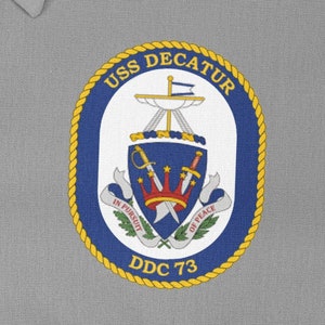 May include: A navy blue and gold embroidered patch with the text "USS DECATUR DDC 73" and a crest featuring a ship, swords, and a crown.