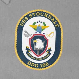 May include: A navy blue and gold circular patch with the text "USS STOCKDALE DDG 106" and a crest featuring an eagle, a trident, and the words "Return with Honour".