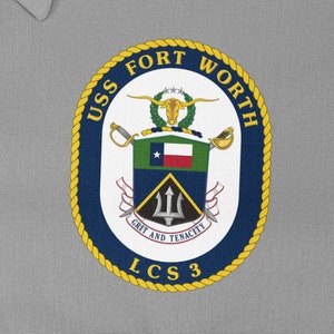 Può includere: Una toppa circolare blu scuro e oro con il testo "USS FORT WORTH LCS 3" e uno stemma che presenta un longhorn del Texas, una bandiera del Texas e un tridente con il testo "GRIT AND TENACITY".