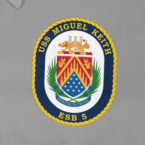 Könnte beinhalten: Ein marineblauer und goldener runder Aufnäher mit dem Text "USS MIGUEL KEITH ESB 5" und einem Wappen mit einem Schild in Rot und Gelb, einem Drachen und einem Banner mit Sternen.