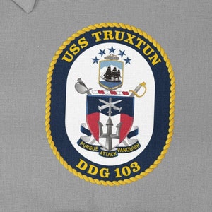 Può includere: Una toppa circolare blu navy e oro con il testo "USS TRUXTUN DDG 103" e uno stemma che presenta una nave, spade incrociate e un'ancora. Lo stemma è circondato da un bordo di corda.
