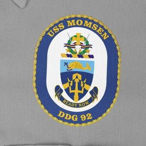 May include: A blue and white circular patch with a gold chain border. The patch has the text "USS MOMSEN DDG 92" and the words "READY NOW" inside a banner. The patch also features a crest with a trident and a dolphin.
