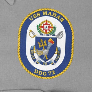 May include: A navy blue and gold circular patch with the text "USS MAHAN DDG 72" and a crest featuring a trident, a torch, and a sword. The crest is surrounded by a rope design.