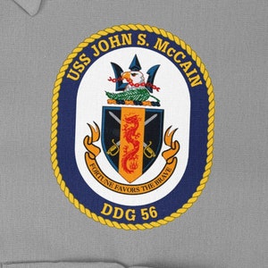 May include: A navy blue and gold circular patch with the text "USS JOHN S. MCCAIN DDG 56" and a crest featuring a dragon, swords, and a bird.