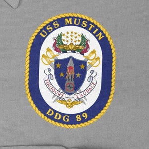 May include: A navy blue and gold embroidered patch with the text "USS MUSTIN DDG 89" and a crest featuring a rocket, stars, and the text "TOUJOURS L'AUDACE".